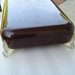 May include: A dark brown rectangular box with a glossy finish and clear plastic feet. The box has a decorative design on the feet.