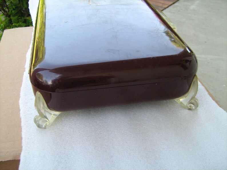 May include: A dark brown rectangular box with a glossy finish and clear plastic feet. The box has a decorative design on the feet.
