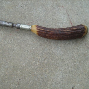 May include: A vintage, metal and antler handled tool with a silver band. The tool has a dark brown antler handle with a silver band.