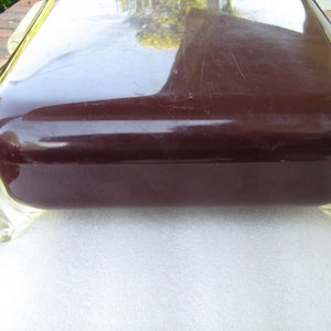 May include: A dark brown rectangular box with a glossy finish and clear plastic feet. The box has a slightly rounded top and is resting on a white surface.