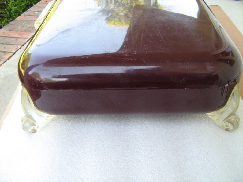 May include: A dark brown rectangular box with a glossy finish and clear plastic feet. The box has a slightly rounded top and is resting on a white surface.
