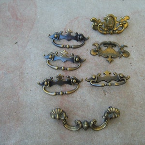 May include: Eight antique cabinet knobs with ornate designs. The knobs are made of brass and have a dark finish. Some of the knobs have a decorative floral design, while others have a more simple design.