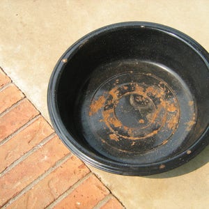 May include: A black metal bowl with a rusty interior. The bowl is round and has a slightly raised rim.