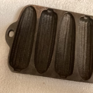 May include: Cast iron corn on the cob baking pan with six individual molds. The pan is dark gray and has a rustic look.