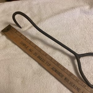 May include: A rusty metal hook with a triangular handle. The hook is about 15 inches long and is measured against a wooden ruler labeled "Sample No. 30 Brass Tip Admanco Wolverine".