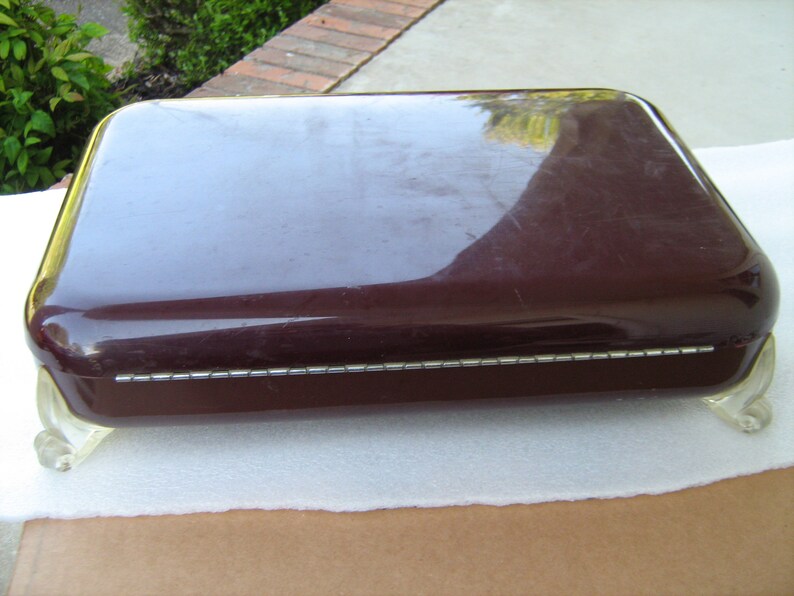 May include: A dark brown rectangular box with a decorative silver trim around the edge. The box has four clear plastic feet.