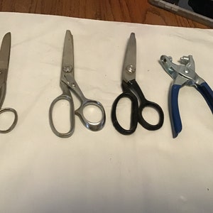Peut inclure: Quatre outils pour la couture et l'artisanat, dont trois paires de ciseaux et une poin&ccedil;onneuse &agrave; &oelig;illets en m&eacute;tal. Deux des ciseaux ont des lames et des poign&eacute;es argent&eacute;es, tandis que la troisi&egrave;me paire a des poign&eacute;es noires. La poin&ccedil;onneuse &agrave; &oelig;illets a des poign&eacute;es bleues.
