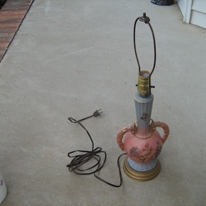 May include: A ceramic table lamp with a pink and blue floral design. The lamp has a gold-colored base and a wire cord.