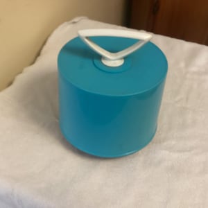 May include: A turquoise blue plastic container with a white handle. The container has a rounded shape and a smooth surface.