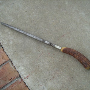 May include: A long, silver steel knife sharpener with a brown antler handle.