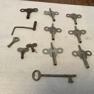 May include: A collection of vintage clock winding keys. The keys are made of metal and have different shapes and sizes. Some of the keys are silver, while others are brass.