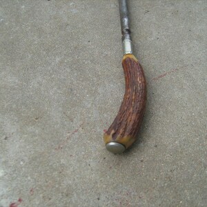 May include: A brown antler handle with a silver band and a metal cap on the end. The handle is attached to a metal rod.