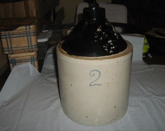 May include: A white ceramic crock with a black lid. The crock has a number "2" written on the front in blue paint.