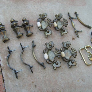 May include: A collection of antique brass cabinet knobs and pulls, including ornate designs with ivory accents, simple loop pulls, and decorative knobs with a fluted design.