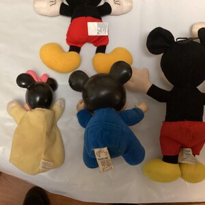 Puede incluir: Una colecci&oacute;n de mu&ntilde;ecos de peluche vintage de Mickey Mouse y Minnie Mouse. Los mu&ntilde;ecos de Mickey visten pantalones cortos rojos, cuerpos negros, zapatos amarillos y guantes blancos. Los mu&ntilde;ecos de Minnie visten vestidos amarillos y lazos rosas. Los mu&ntilde;ecos est&aacute;n sobre una superficie blanca.