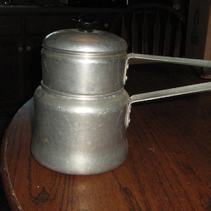 May include: A silver double boiler with two handles. The top pot has a black knob on the lid.