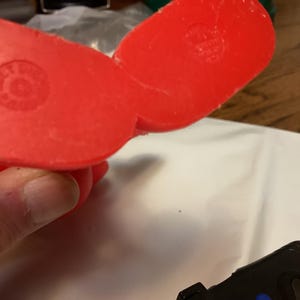 May include: Close-up of the underside of a bright red plastic object. The object has a rounded shape with a circular indentation on each side. The object is being held by a person's hand.