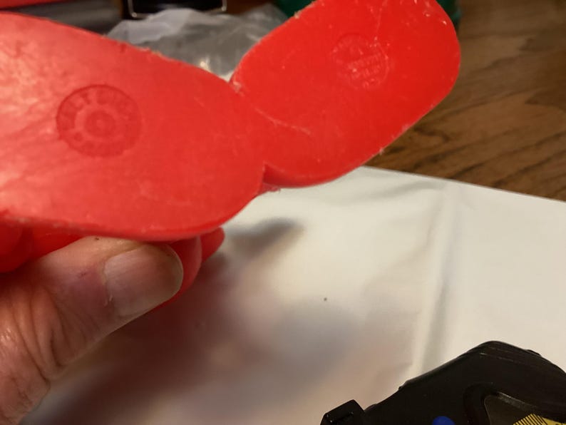 May include: Close-up of the underside of a bright red plastic object. The object has a rounded shape with a circular indentation on each side. The object is being held by a person's hand.