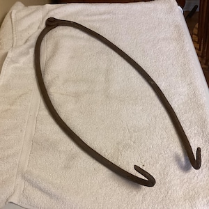 May include: A rusty metal hook with two loops at the end. The hook is bent into a U-shape and is lying on a white towel.