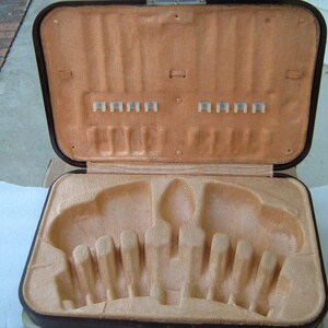May include: A brown leatherette case with a beige velvet interior. The case has a hinged lid and is designed to hold cutlery. The interior has slots for forks, knives, and spoons.