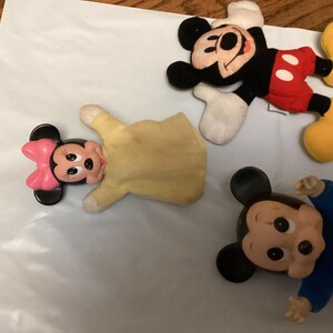 Puede incluir: Una colecci&oacute;n de peluches de Mickey Mouse y Minnie Mouse. Mickey Mouse viste su atuendo cl&aacute;sico con pantalones cortos rojos, orejas negras y zapatos amarillos. Minnie Mouse tiene un lazo rosa. Un Mickey Mouse lleva un traje azul.