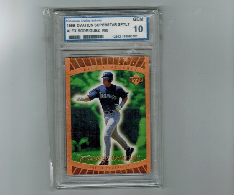 May include: A graded baseball card featuring Alex Rodriguez, a Seattle Mariners player, in a green and orange frame. The card is graded GEM 10 and is from the 1999 Ovation Superstar Spotlight series.