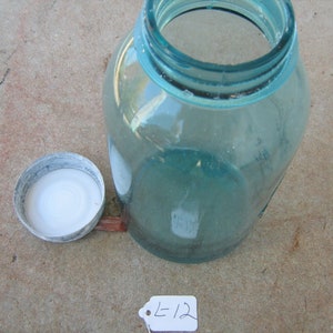 May include: A vintage aqua blue glass jar with a white lid. The jar has a wide mouth and is made of thick glass. The lid is made of metal and has a smooth surface.