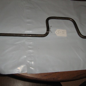 May include: A vintage, metal lug wrench with a curved handle and a socket end. The wrench has a dark, aged appearance, with a small tag labeled "S-5" attached to the handle. The tool is designed for automotive use.