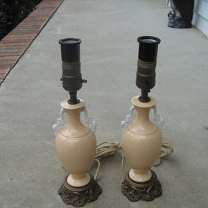 May include: Two ceramic table lamps with white accents and gold bases. The lamps have a cream colored body and a black lampshade.