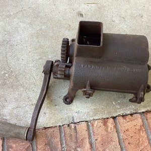 May include: Antique cast iron meat grinder with a wooden handle. The grinder has a square hopper and a crank handle. The text "Enterprise No. 8" is visible on the side of the grinder.