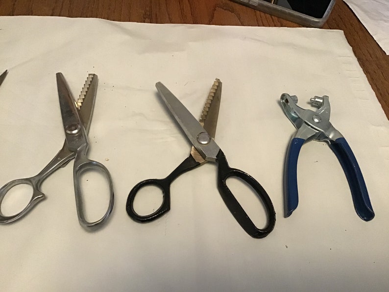 Peut inclure: Quatre outils pour la couture et l'artisanat, dont deux paires de ciseaux &agrave; tissu argent&eacute;s et noirs &agrave; lames dentel&eacute;es et une poin&ccedil;onneuse &agrave; &oelig;illets en m&eacute;tal bleu.