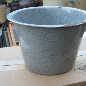 May include: A gray metal bucket with a speckled finish. The bucket is sitting on a cardboard box.