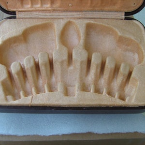 May include: A brown leatherette case with a beige velvet interior. The case has a series of slots for holding cutlery or other utensils.