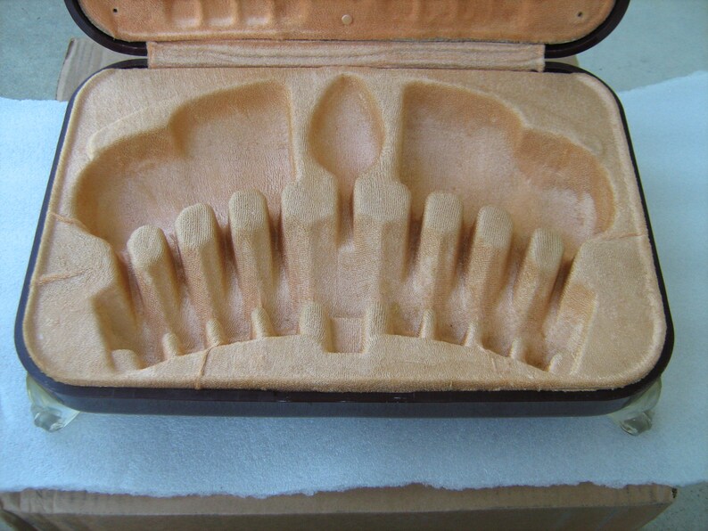 May include: A brown leatherette case with a beige velvet interior. The case has a series of slots for holding cutlery or other utensils.