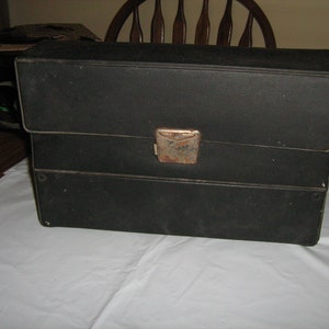 May include: A black, rectangular, two-piece carrying case with a metal latch. The case has a worn, vintage look.