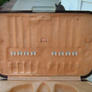 May include: A brown leather case with a beige interior and multiple slots for holding items. The case is open and the interior is visible.