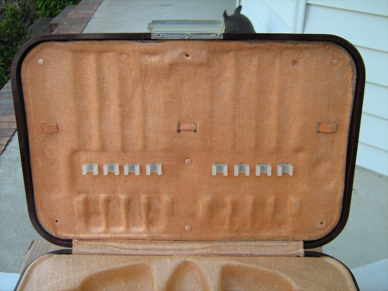 May include: A brown leather case with a beige interior and multiple slots for holding items. The case is open and the interior is visible.