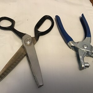 Peut inclure: Une paire de ciseaux &agrave; tissu argent&eacute;s avec des poign&eacute;es noires et un poin&ccedil;on &agrave; &oelig;illets en m&eacute;tal bleu.