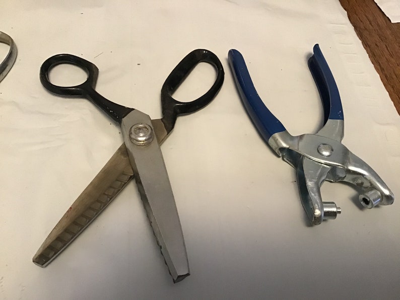 Peut inclure: Une paire de ciseaux &agrave; tissu argent&eacute;s avec des poign&eacute;es noires et un poin&ccedil;on &agrave; &oelig;illets en m&eacute;tal bleu.