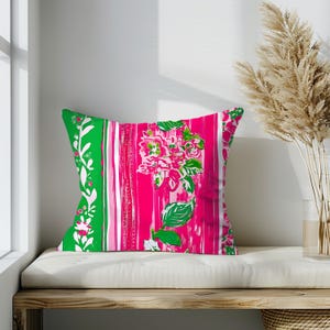 May include: A pink and green patterned cushion with a floral design. The cushion is on a white bench with a wooden base.