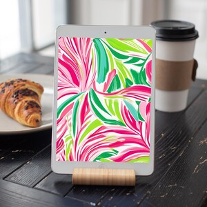 May include: A tablet displaying a digital illustration of pink, green and blue abstract floral patterns on a white background.