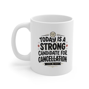 May include: A white ceramic mug featuring a black graphic design with the text "TODAY IS A STRONG CANDIDATE FOR CANCELLATION" in a bold, stylised font. The design includes a small, grumpy face icon at the top and red star accents on the sides.