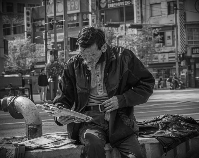 Black and white photo Old Man Reading Newspaper on Busy Street - Seoul, South Korea - Urban Photo Print