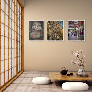 Puede incluir: Tres fotografías enmarcadas cuelgan de una pared beige. Las fotos representan escenas urbanas, incluyendo una calle con letreros, un edificio con andamios y una concurrida escena callejera con gente. Una mesa baja de madera con una tetera y tazas está frente a la pared.