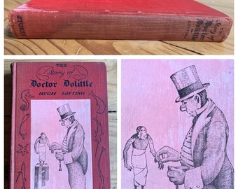 May include: A red hardback book with the title "The Story of Doctor Dolittle" by Hugh Lofting. The cover features a black and white illustration of Doctor Dolittle with a monkey.