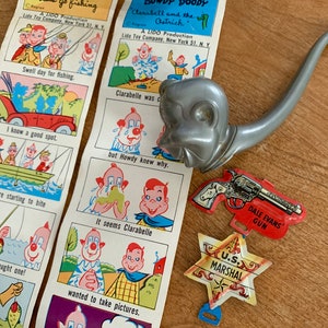 May include: A set of vintage toy accessories featuring a silver toy pipe, a red toy gun with the text "Dale Evans' Gun", and a red and white star-shaped toy badge with the text "U.S. Marshal".