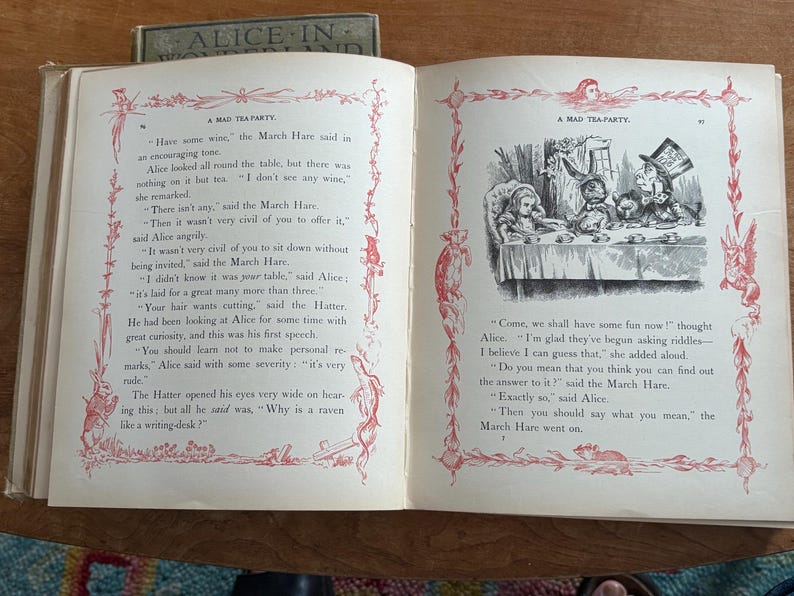 May include: Open book with illustrations and text from "Alice in Wonderland." The pages show a drawing of a tea party with Alice, the Mad Hatter, and the March Hare. The text includes the phrase "A Mad Tea Party."