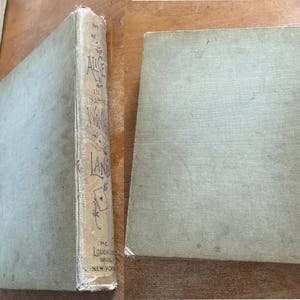 May include: Two antique books with light green covers. The spine of one book reads "Alice's Wonderland" with decorative illustrations and the publisher's name. The other book is lying flat, showing its cover.