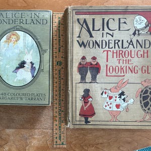 May include: Two vintage books, "Alice in Wonderland" and "Alice in Wonderland & Through the Looking-Glass", with illustrations. The first book is green with an oval illustration of Alice and a rabbit. The second book has illustrations of characters from the story.