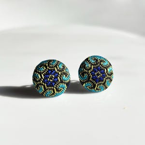 May include: A pair of blue and gold earrings with a geometric pattern. The earrings are made of fabric and have a round shape.
